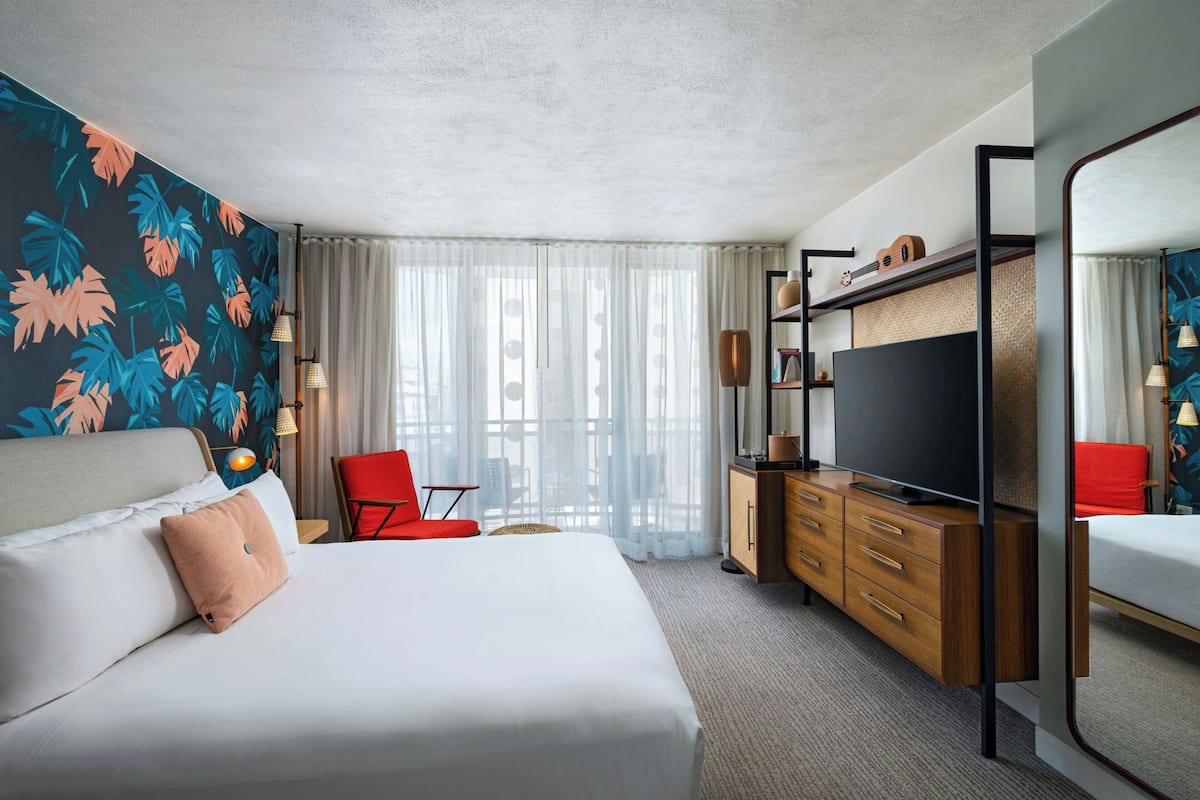A modern hotel room with a large bed, a TV, a wooden dresser, and a red chair.