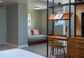 A modern bedroom with a bunk bed, a desk with drawers, a wicker chair, and a sofa with cushions.