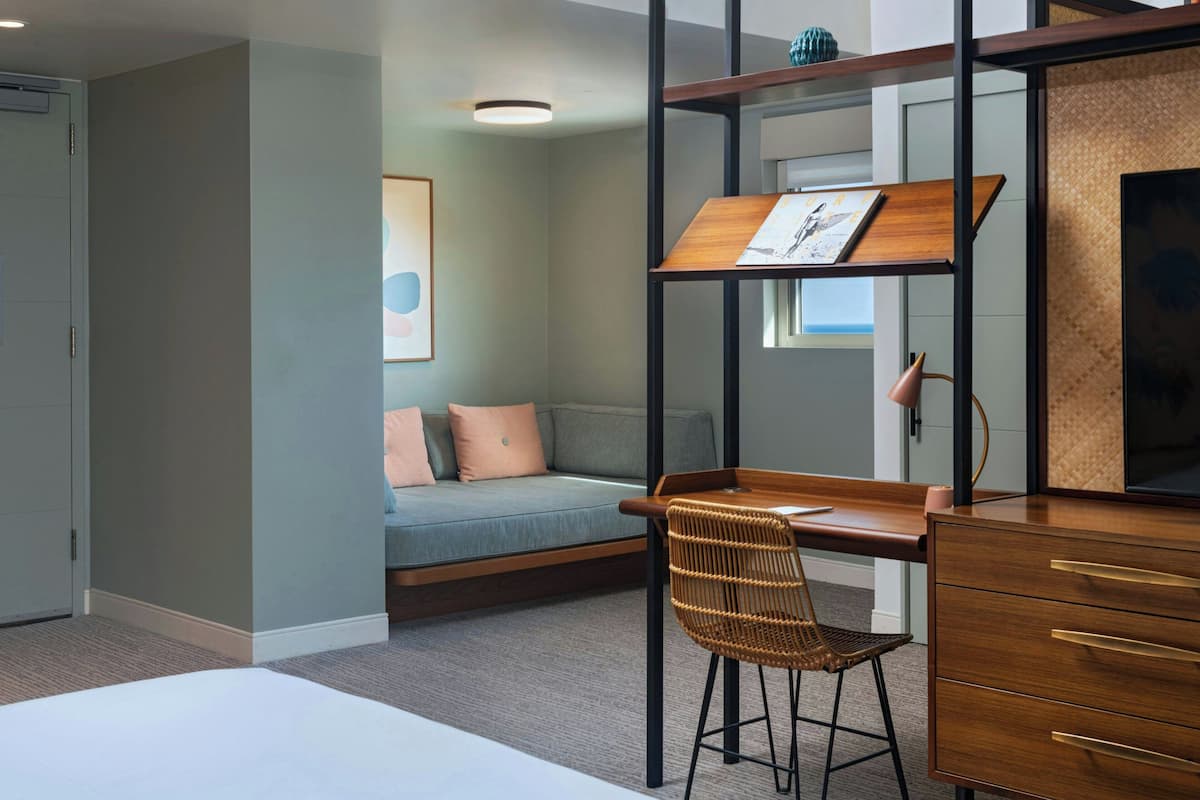 A modern bedroom with a bunk bed, a desk with drawers, a wicker chair, and a sofa with cushions.