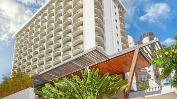 Un hotel moderno con varios balcones, un espacio al aire libre cubierto con plantas y una fachada con un cartel.