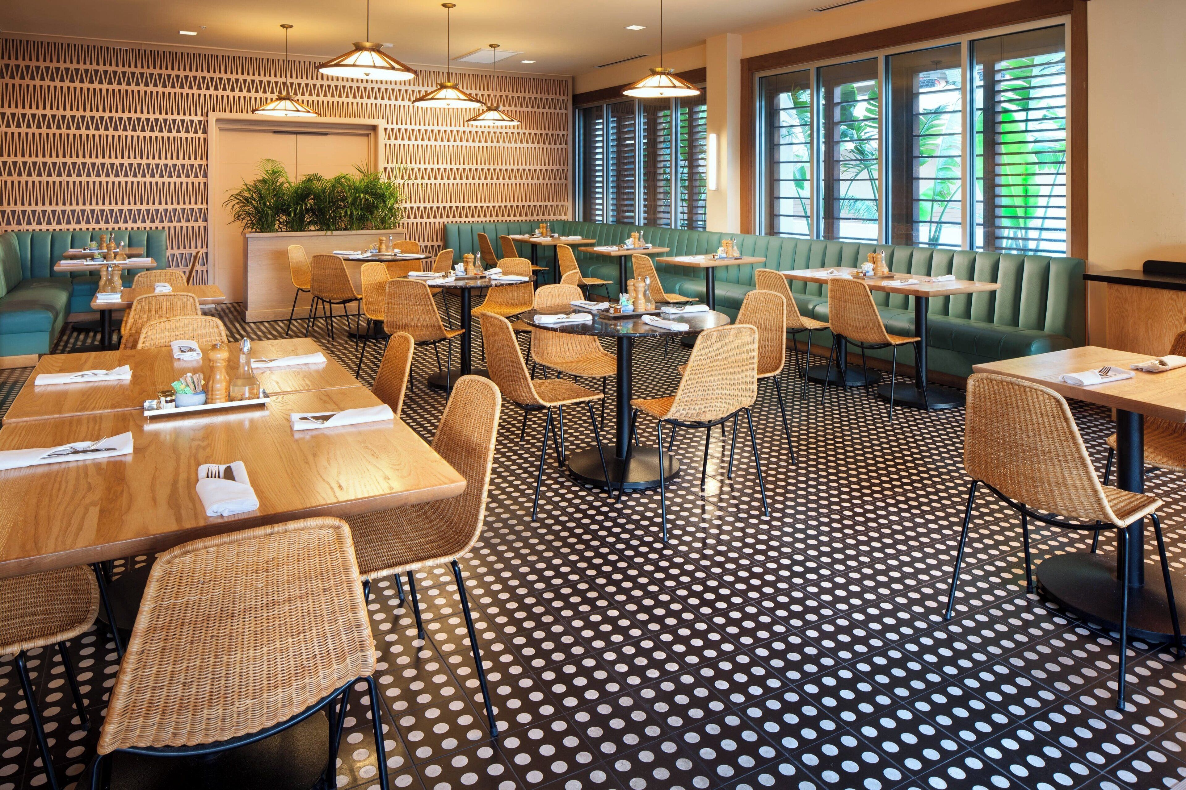 A restaurant with a patterned floor, green booths, and wicker chairs.