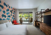 A hotel room with a bed, a desk, a TV, and a view of the outdoors through a sliding glass door.