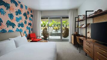 Ein Hotelzimmer mit Bett, Schreibtisch, Fernseher und Blick ins Freie durch eine Glastür.