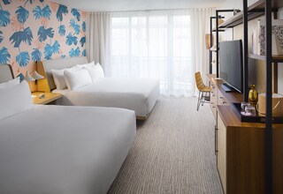 A hotel room with two beds, a TV, a desk with a lamp, and a bookshelf.