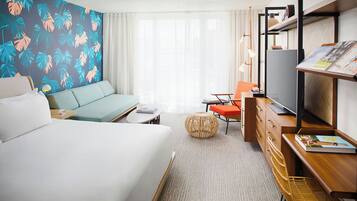 A hotel room with a bed, a sofa, a desk with a computer, a chair, and a television.