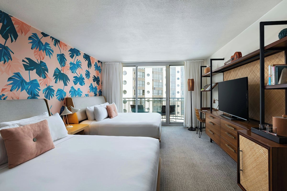 A hotel room with two beds, a TV, a bookshelf, and a balcony with a view of buildings.