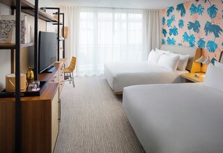 A hotel room with two beds, a desk with a TV, a chair, and a large window with curtains.