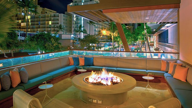 A modern outdoor lounge area with a fire pit, seating, and a view of the cityscape. - The Laylow Waikiki, Autograph Collection (Honolulu)