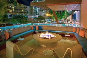 A modern outdoor lounge area with a fire pit, seating, and a view of the cityscape. - The Laylow Waikiki, Autograph Collection (Honolulu)