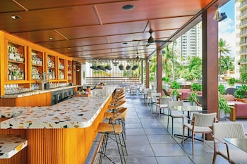 A wall with a wooden panel and a grid of white knobs, with potted plants in front. at The Laylow Waikiki, Autograph Collection