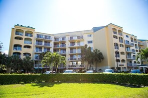 A multi-story hotel with balconies, a parking area, and a well-maintained lawn.