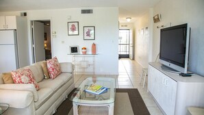 A living room with a sofa, coffee table, TV, and a kitchen area in the background.