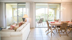 A living room with a white sofa, a dining table with chairs, and a balcony with a chair.