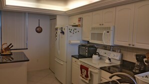 A compact kitchen with white cabinets, a refrigerator, a microwave, a stove, and a kettle. - South Seas Tower 3 1905 (Marco Island)