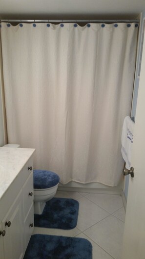 A bathroom with a white toilet, a blue bath mat, a white sink with a marble countertop, and a shower curtain with blue dots.