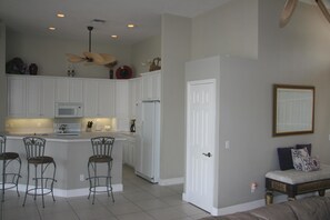 A modern kitchen with white cabinets, a central island with bar stools, a ceiling fan, and a refrigerator.
