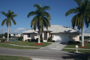 A single-story house with a tiled roof, a front garage, and a well-maintained lawn with palm trees.