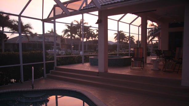 A pool area with a glass enclosure, palm trees, and a view of a building in the background. - 431 Edgewater Ct (Marco Island)