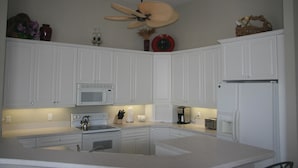 A modern kitchen with white cabinets, a microwave, a stove, a coffee maker, and a ceiling fan. - 431 Edgewater Ct (Marco Island)