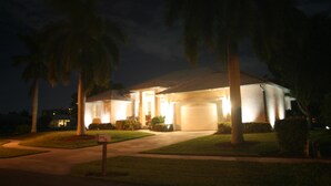 A residential house at night with a well-lit front entrance, surrounded by palm trees and a lawn. - 431 Edgewater Ct (Marco Island)