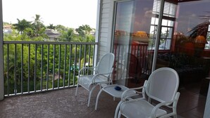 A balcony with white chairs and a glass door. - Olde Marco Inn 401 (Marco Island)