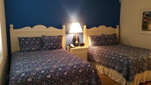 A room with two beds, each with patterned bedding, a nightstand with a lamp, and a painting on the wall. - Olde Marco Inn 401 (Marco Island)