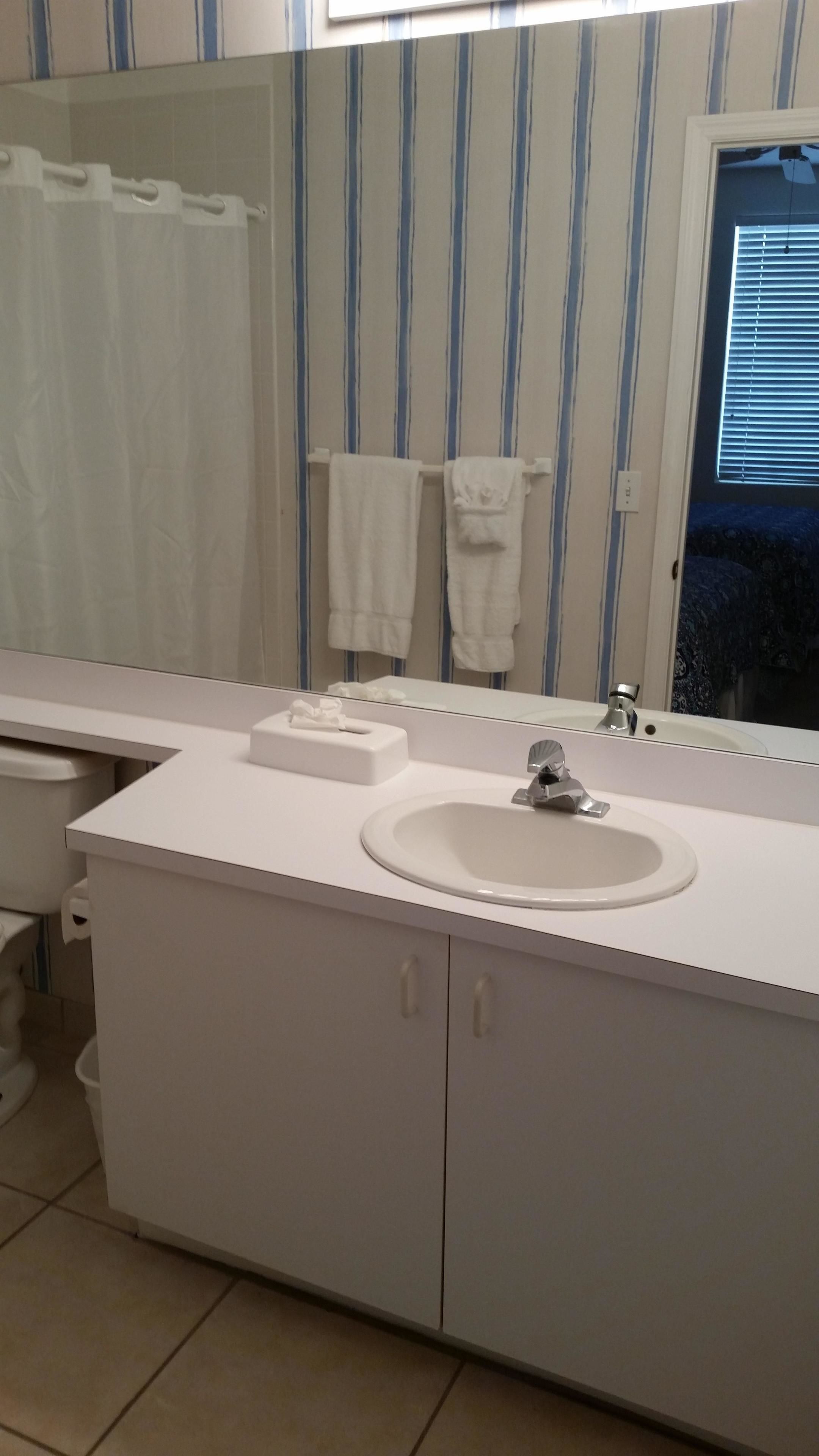 A bathroom with a white vanity, a sink, and a mirror. There are striped towels hanging on a rack.