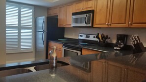 A kitchen with wooden cabinets, a stainless steel refrigerator, a microwave, an oven, and a coffee maker. - Grandview 310 (Marco Island)