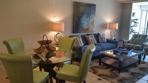 A modern living room with a blue sofa, green armchairs, a glass coffee table, and two lamps. - Grandview 310 (Marco Island)