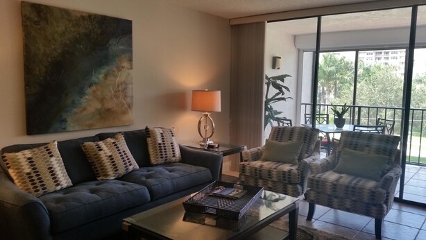 A living room with a sofa, armchairs, a coffee table, a lamp, and a large painting. - Grandview 310 (Marco Island)