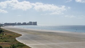 A wide, empty beach with a clear sky and distant buildings.