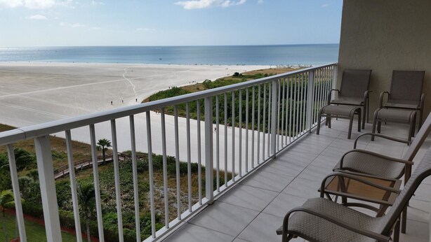 A balcony with a view of a beach and ocean. There are chairs and a railing.