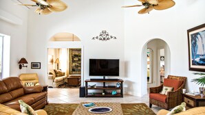 A spacious living room with a large TV, leather sofas, and two ceiling fans. - 1372 Leland Way (Marco Island)