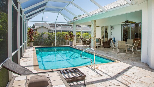 A covered outdoor swimming pool with a glass ceiling, surrounded by patio furniture and a dining area. - 1372 Leland Way (Marco Island)