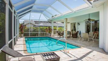 A covered outdoor swimming pool with a glass ceiling, surrounded by patio furniture and a dining area.