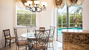 A dining area with a round table, six chairs, and a chandelier. - 1372 Leland Way (Marco Island)