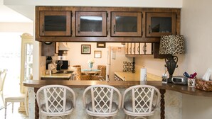 Cucina con mobili in legno, un angolo bar con tre sedie in vimini e una lampada decorativa.