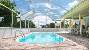 Una piscina coperta con vista sul cielo attraverso un tetto in vetro, circondata da un patio in mattoni e mobili da esterno bianchi.