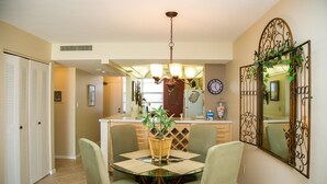Zona pranzo con tavolo in vetro, quattro sedie, un lampadario e uno specchio decorativo.