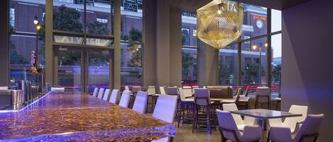 A modern restaurant with a long communal table, white chairs, and a unique geometric light fixture.