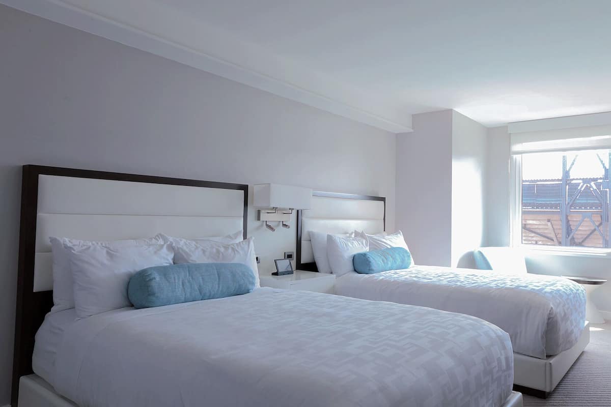 A hotel room with two beds, a desk, and a window with a view of a building.