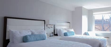 Een hotelkamer met twee bedden, een bureau en een raam met uitzicht op een gebouw.