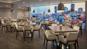 A modern restaurant with multiple dining tables and chairs, a cityscape mural on the wall, and pendant lighting. - Hotel VIA (San Francisco)
