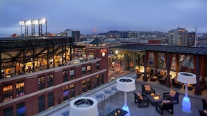 A rooftop bar with outdoor seating, a view of the cityscape, and a clock tower in the background. - Hotel VIA (San Francisco)