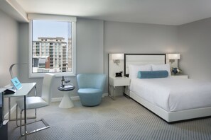 A modern hotel room with a large bed, a desk with a laptop, a chair, and a small table with a bottle and glasses.