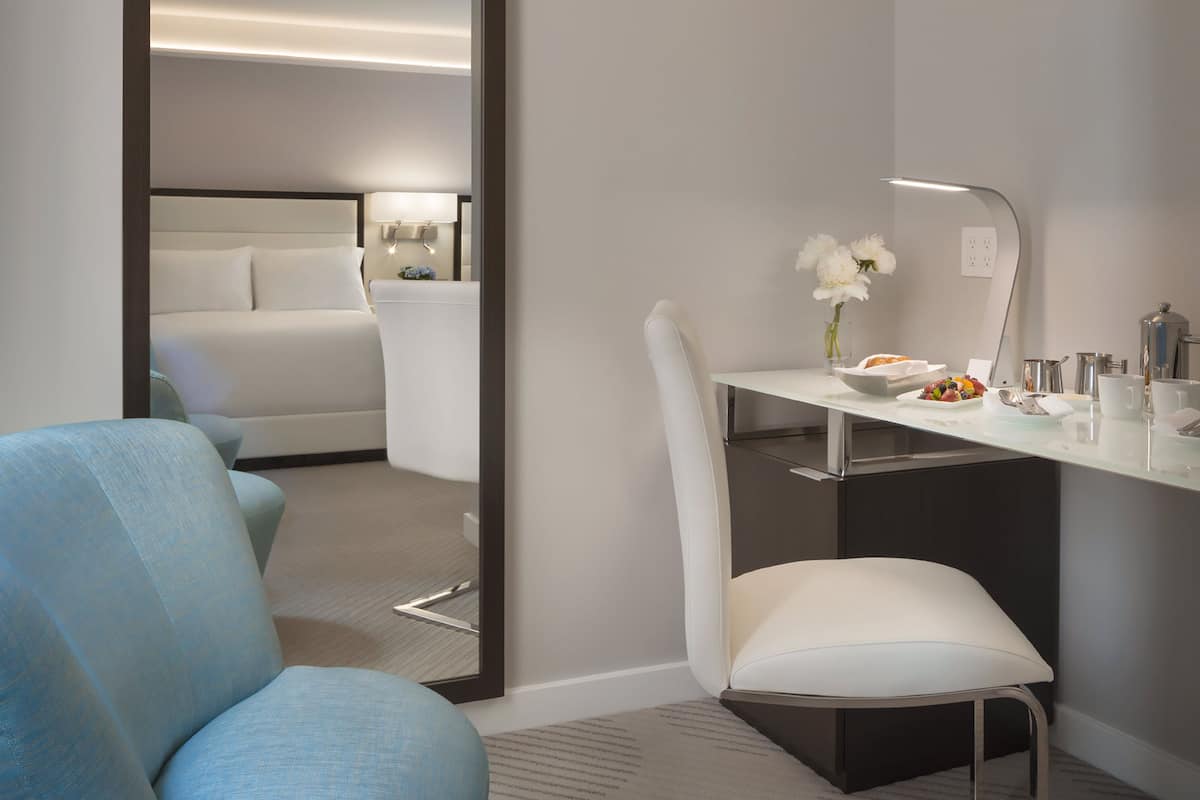 A hotel room with a bed, a desk with a chair, a mirror, and a vase with flowers.