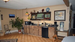 A kitchen with wooden cabinets, a dishwasher, a microwave, and a water dispenser. There is a potted plant and a chair in the room. - Alaska Grizzly Lodge (Fairbanks)