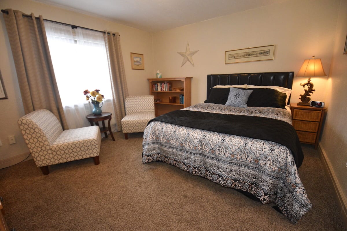 Un dormitorio con cama, dos sillas, una estantería y una decoración con estrellas en la pared.