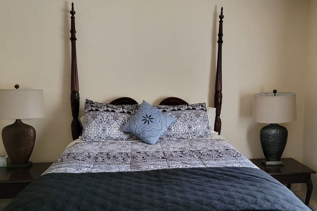 Una cama con dosel, ropa de cama estampada y una almohada decorativa.