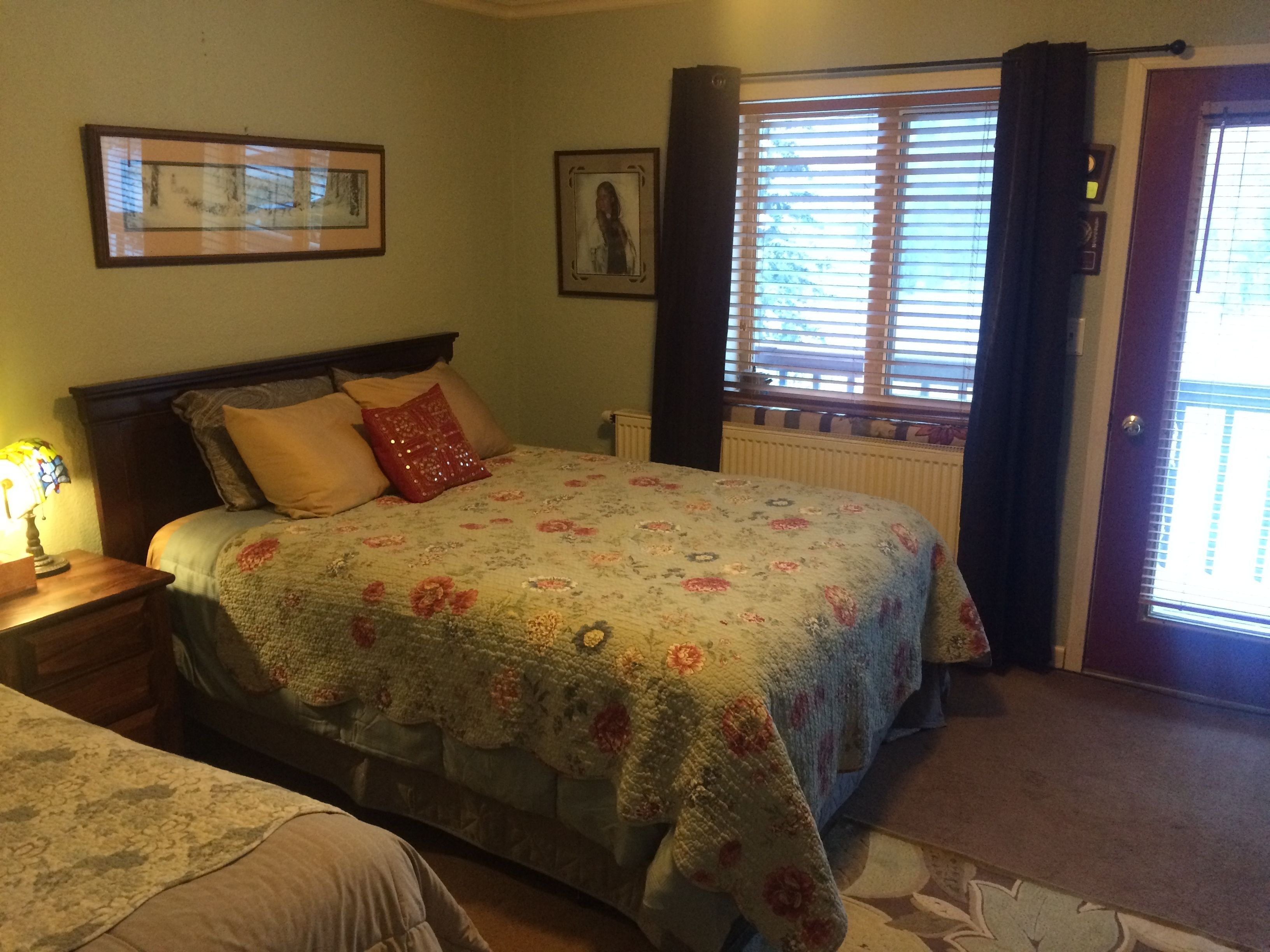 A bedroom with a bed, a nightstand, a window with curtains, and a door.